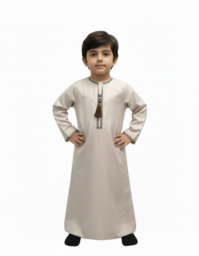 Child wearing a light brown Omani thobe with dark embroidery and a tassel.