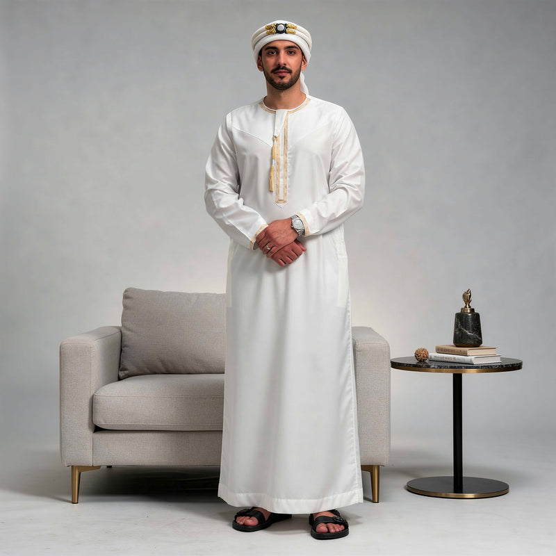 Model wearing a white Omani thobe with gold-tone embroidery and a tassel.