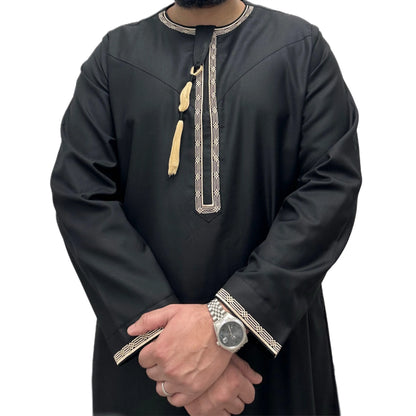 Model wearing black Omani thobe with gold embroidery with arms crossed like traditional front pose.